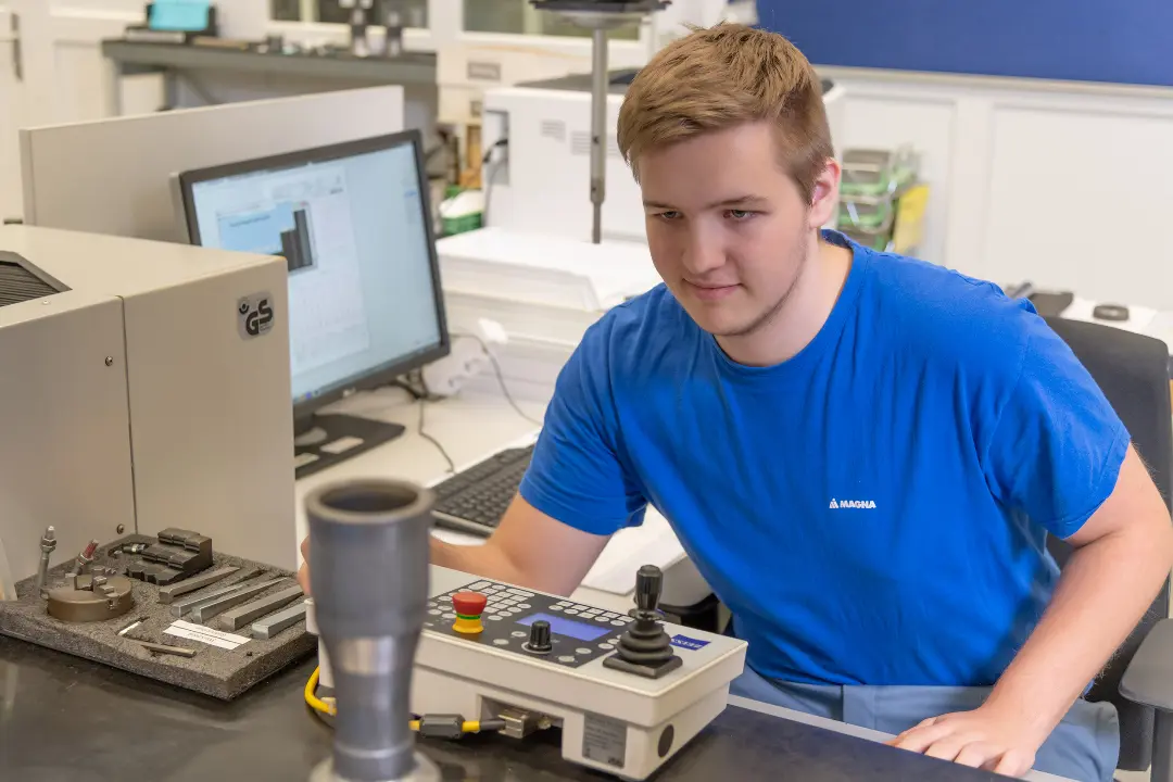 Technician using measurement equipment in a lab with a computer nearby