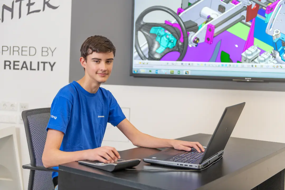 Young technician working on a laptop with a CAD design on a screen in the background