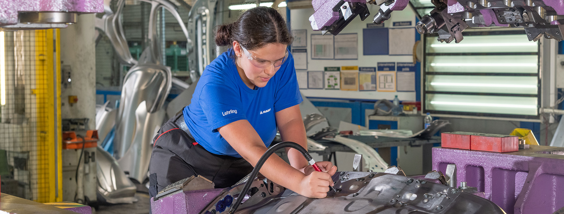 Worker in a blue shirt using tools to assemble a large metal automotive part