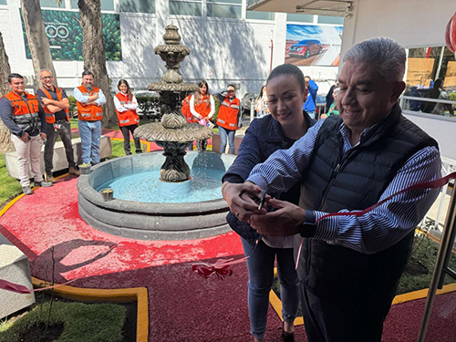 Miguel Arellano and an employee smiling as they cut a ribbon in front of a decorative fountain. Employees in orange vests are standing in the background.