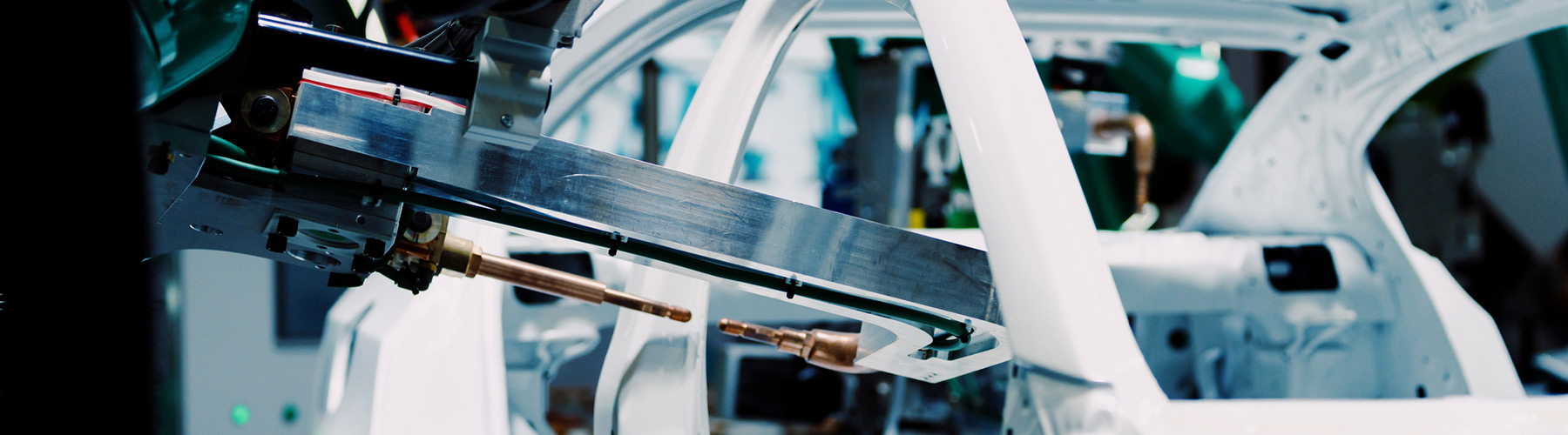 A robotic arm in a factory welds a white car frame, showcasing advanced automated manufacturing processes in an industrial setting.