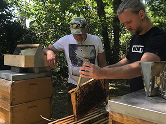 Alessandro Heuberger with his grandfather standing beside their bee hives in a field