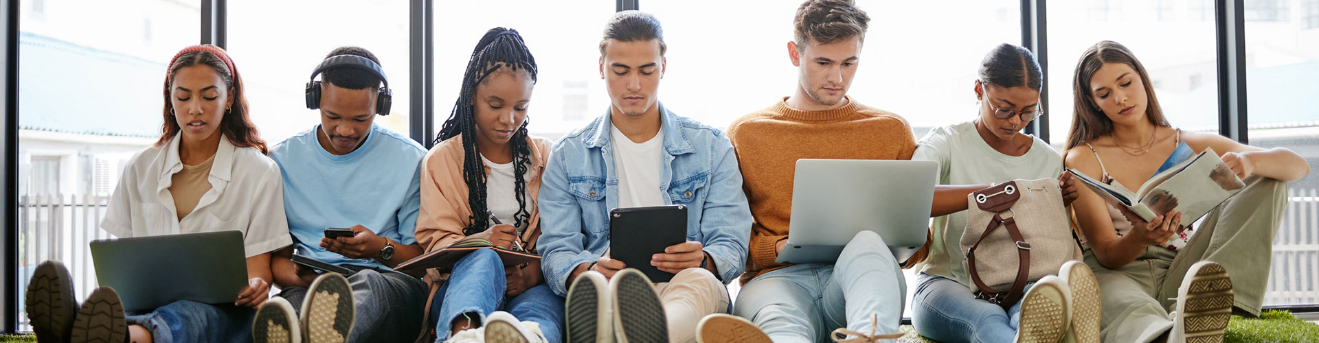 Group of students sitting together using various forms of mobile devices and reading.